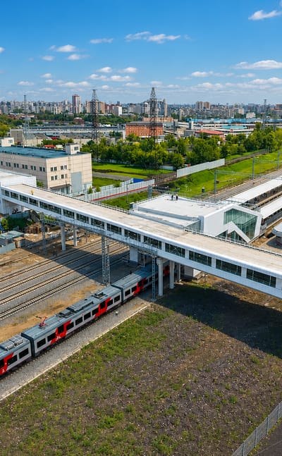Aerial of a modern railway station with pedestrian overpass and commuter train in Kotlovka, Moscow, with the city skyline beyond