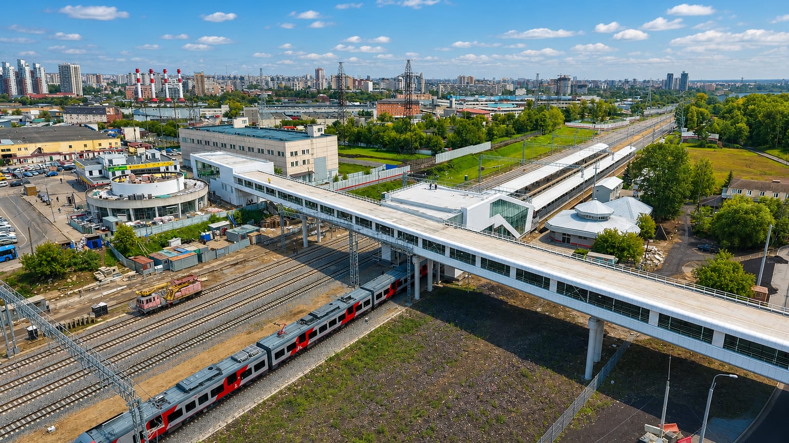 Aerial of a modern railway station with pedestrian overpass and commuter train in Kotlovka, Moscow, with the city skyline beyond