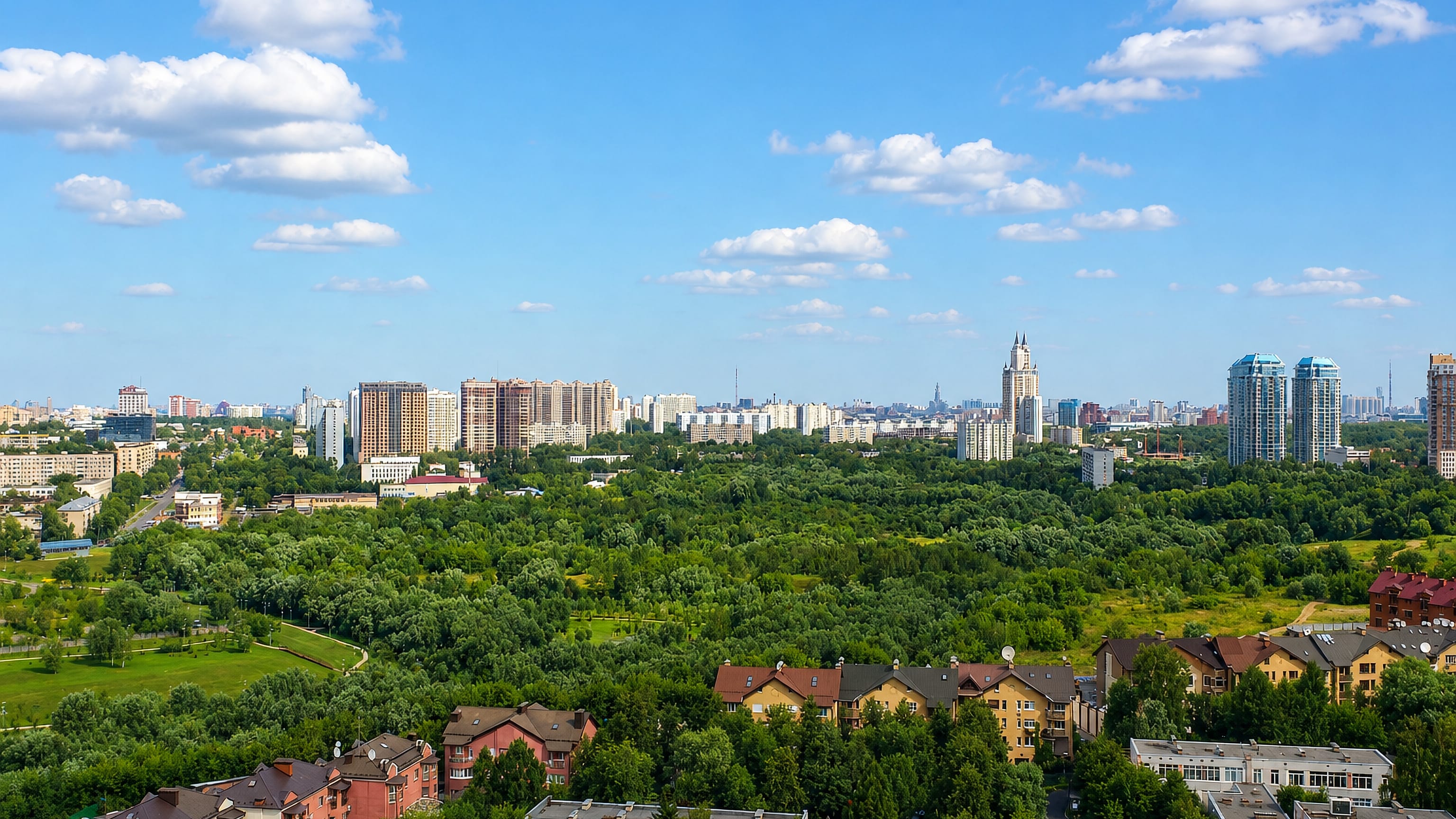Aerial view over the leafy residential blocks of Matveyevskoye with a Stalin-era tower and distant Moscow skyline