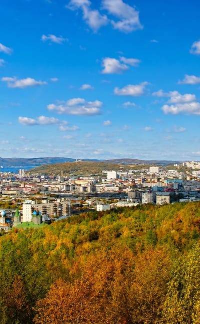 Murmansk spread over hills above the Kola Bay port, framed by golden autumn forest.