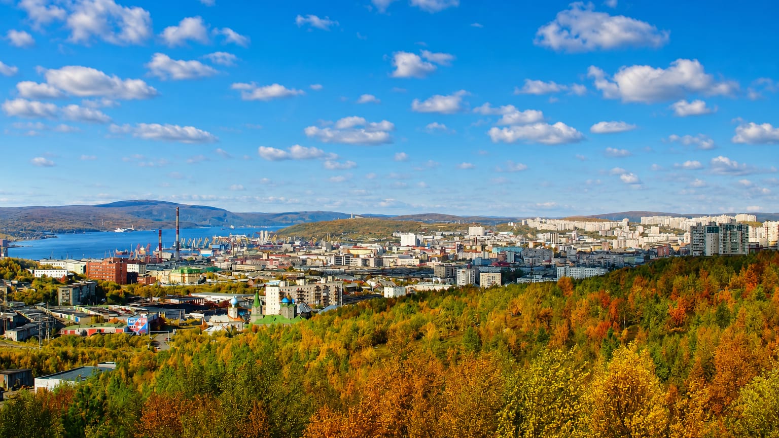 Murmansk spread over hills above the Kola Bay port, framed by golden autumn forest.