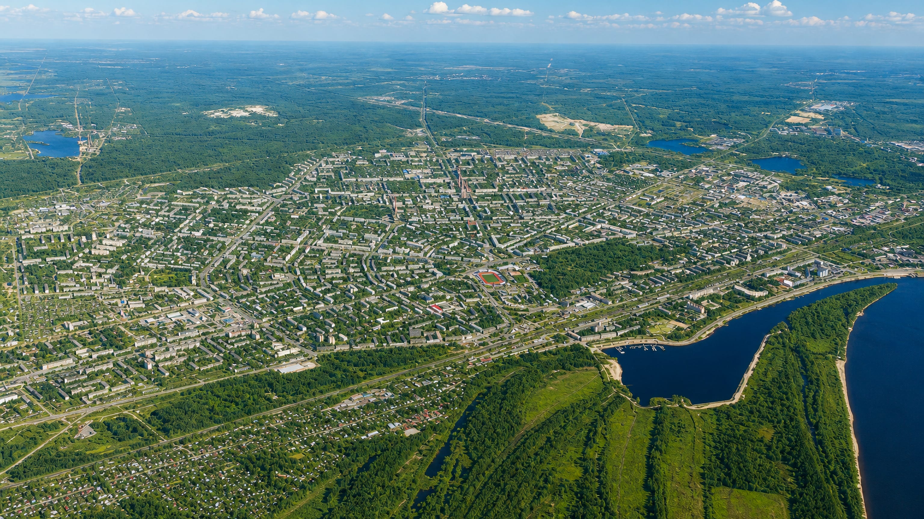 Aerial view of Dzerzhinsk, its low-rise blocks and grid streets ringed by pine forest beside a wide river.