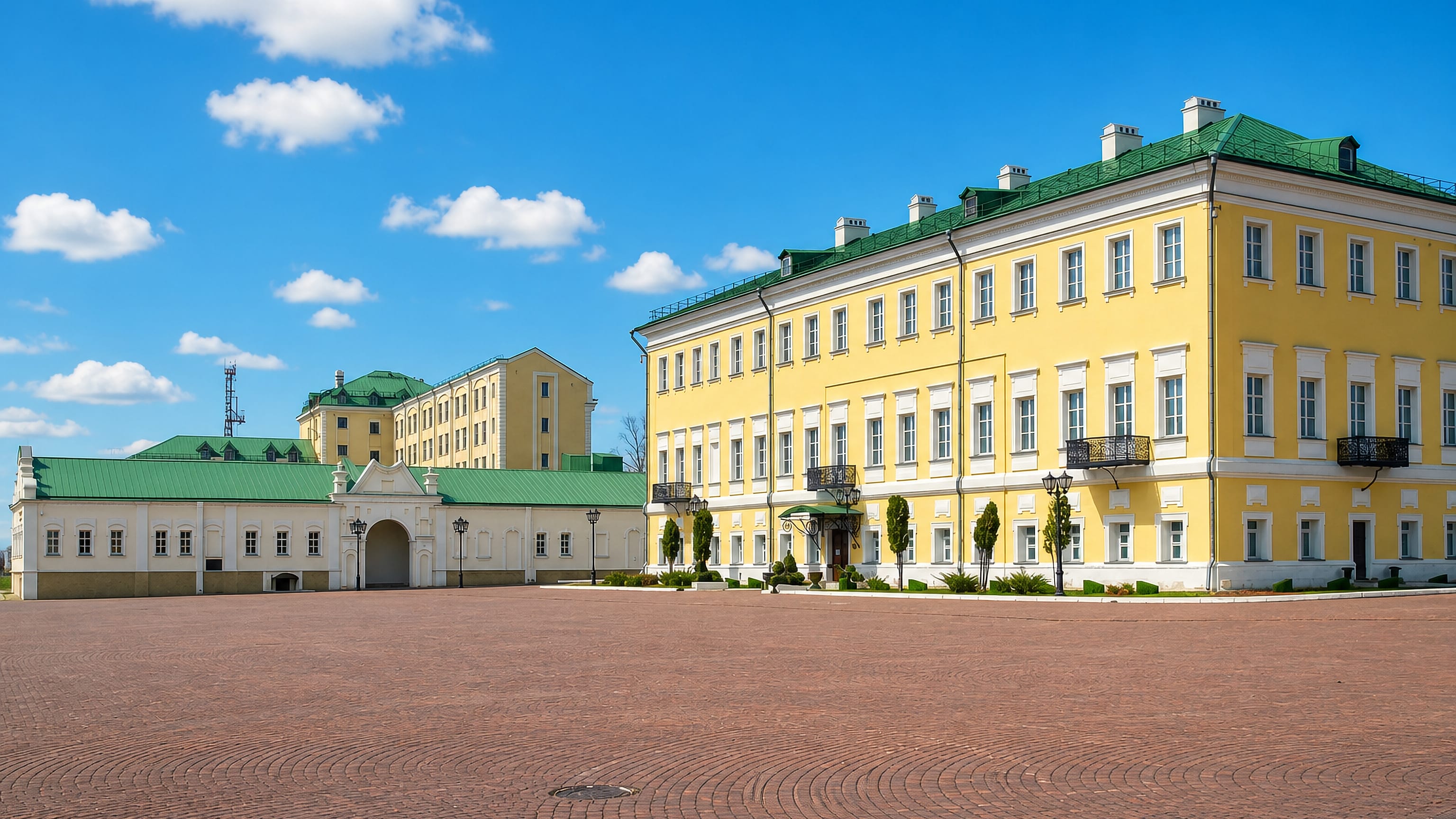 Yellow neoclassical manor house and gatehouse ranged around a brick-paved square in Vyksa, Russia.