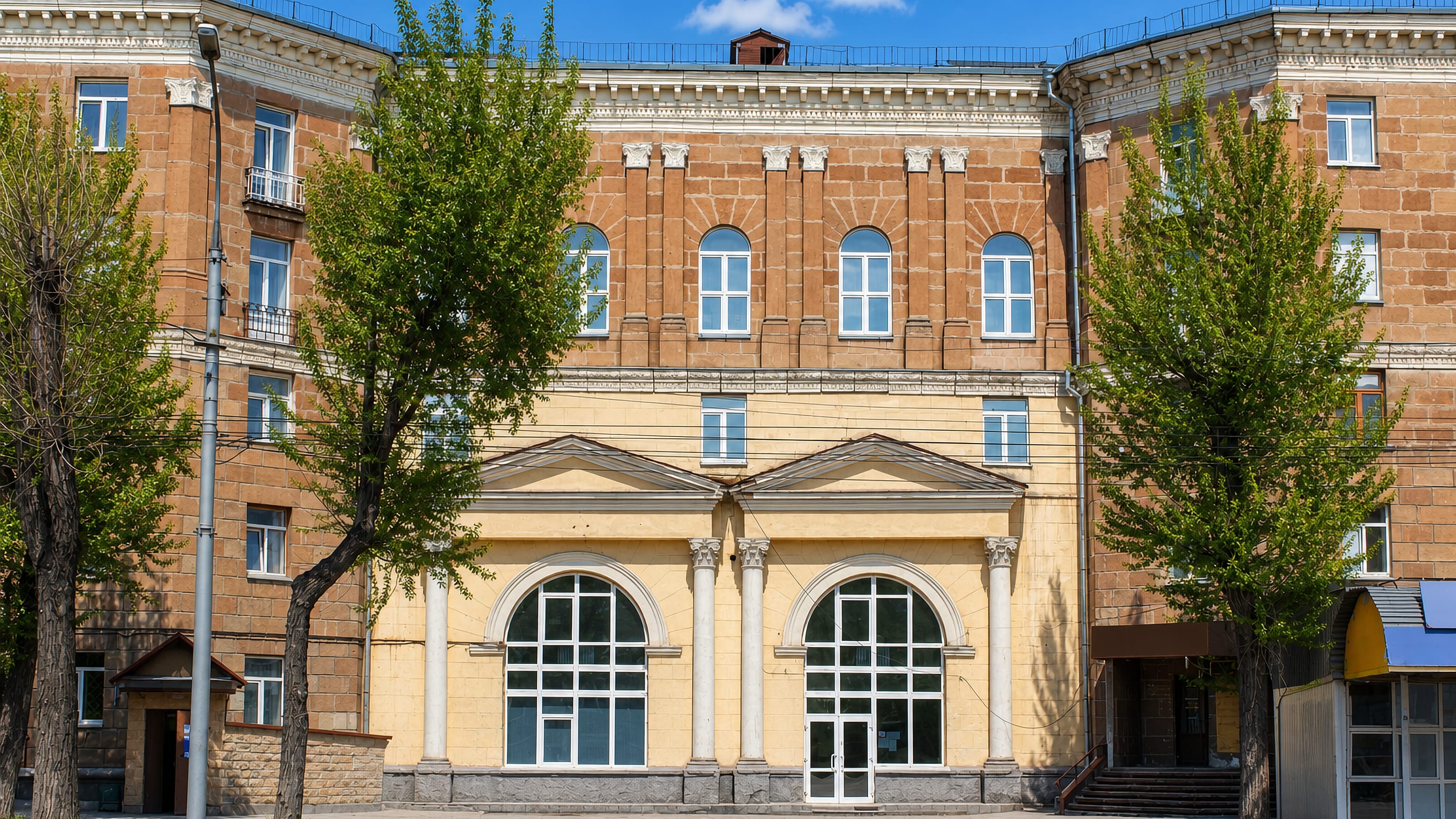 Stalin-era brick apartment block with arched shopfronts on a tree-lined street in Dzerzhinsky District, Novosibirsk