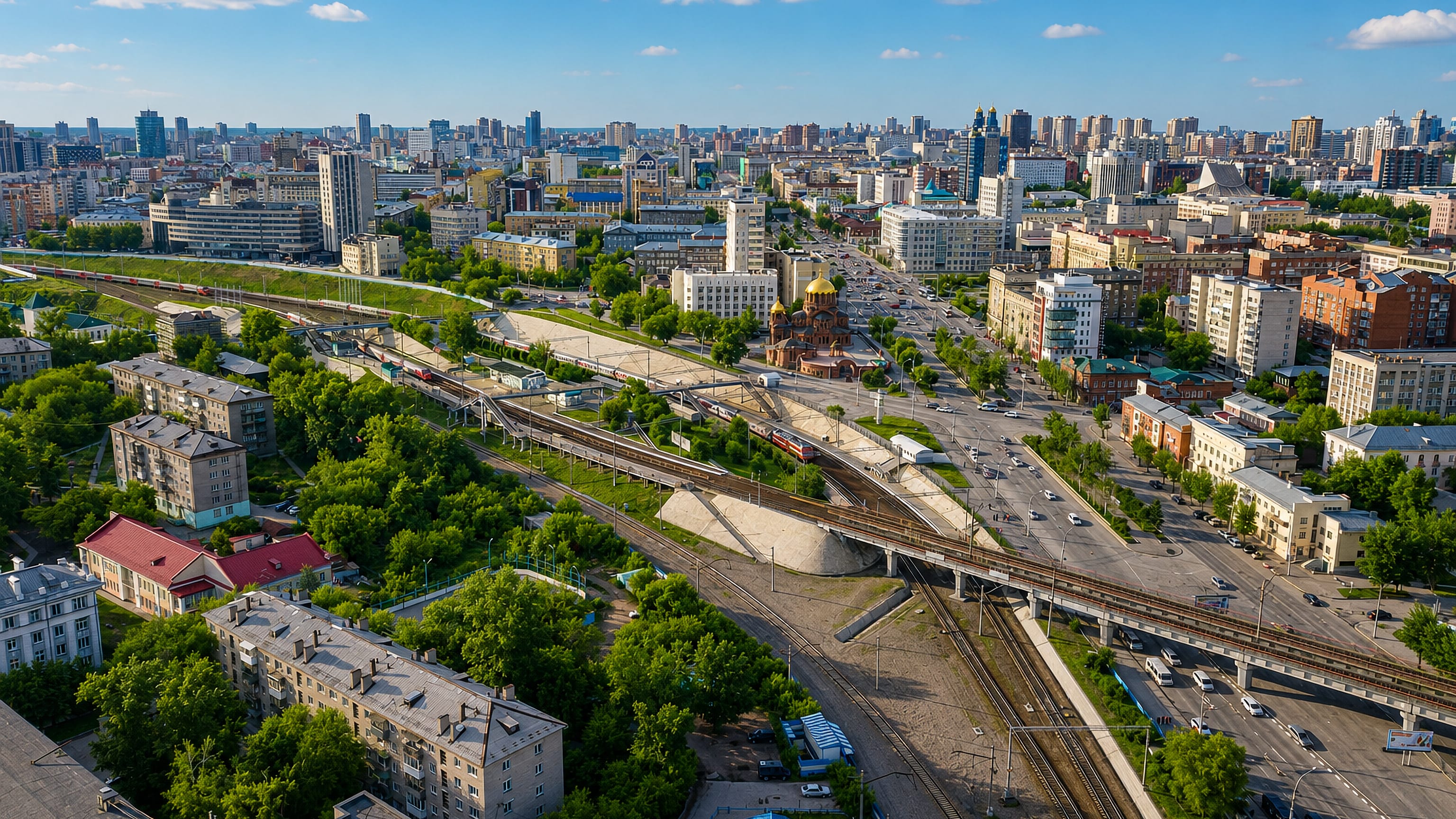 Aerial view of central Novosibirsk with rail lines, a road interchange, a golden-domed church and a dense mid-rise skyline.