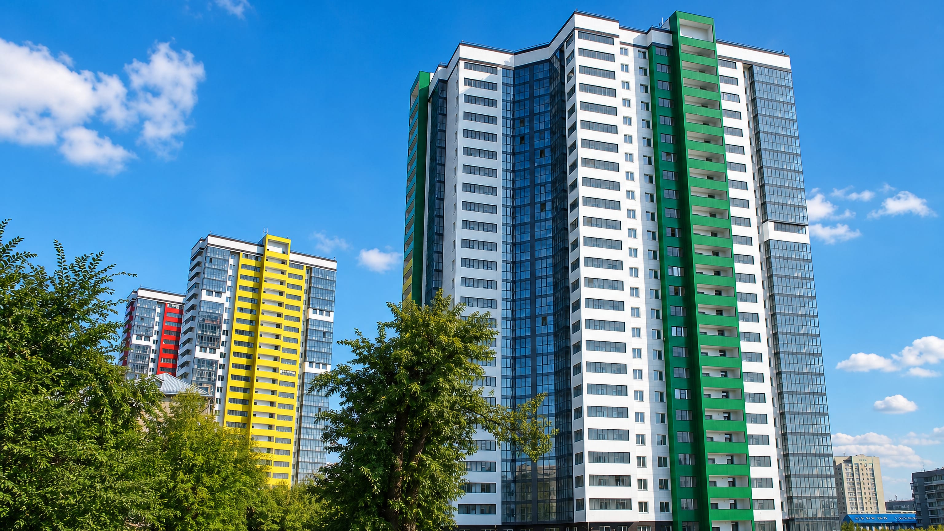 Colourful new high-rise apartment towers above trees and parked cars in Kalininsky City District, Novosibirsk.