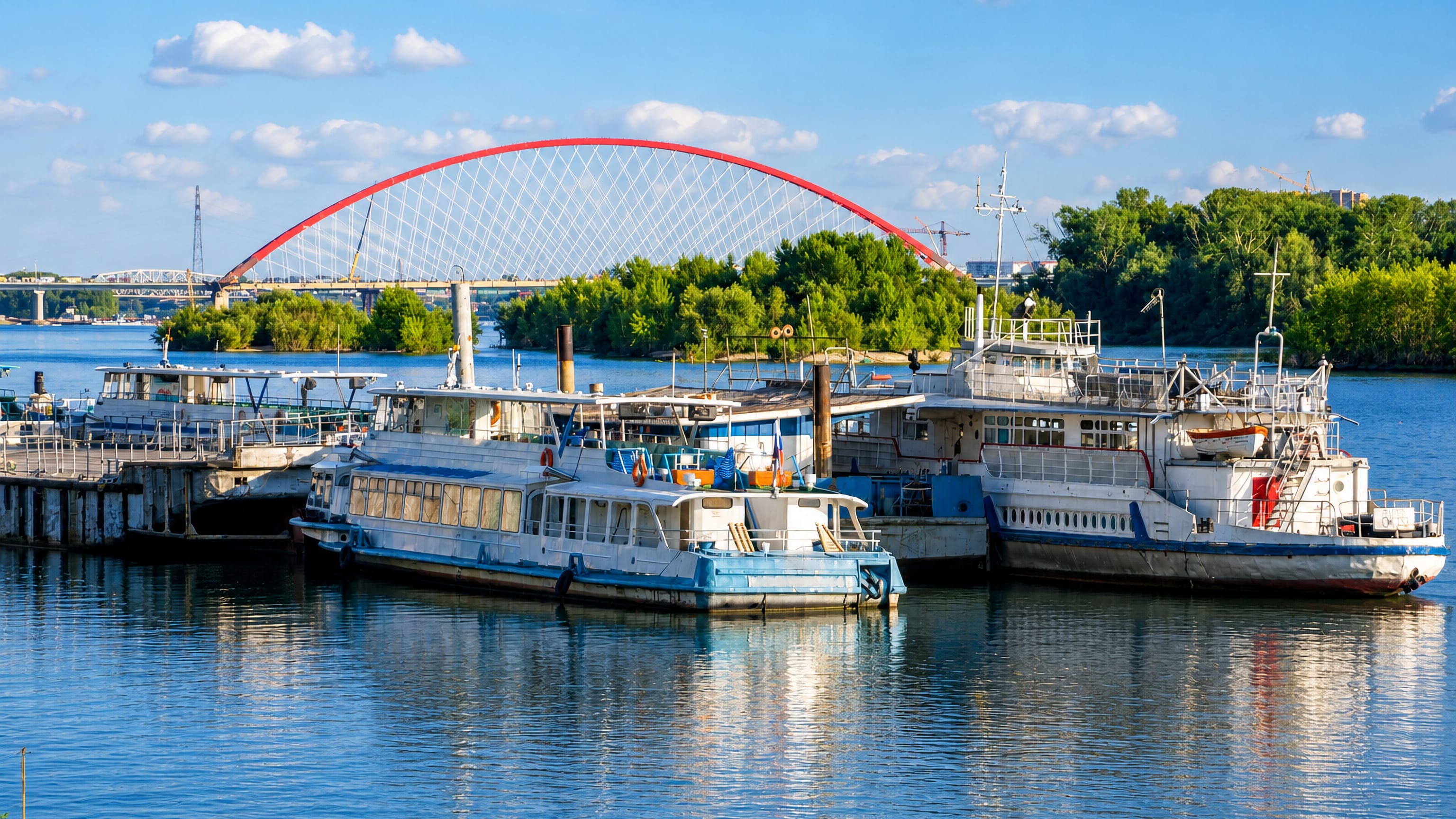 Moored river boats on the Ob with the red arch of the Bugrinsky Bridge behind, Oktyabrsky district, Novosibirsk.