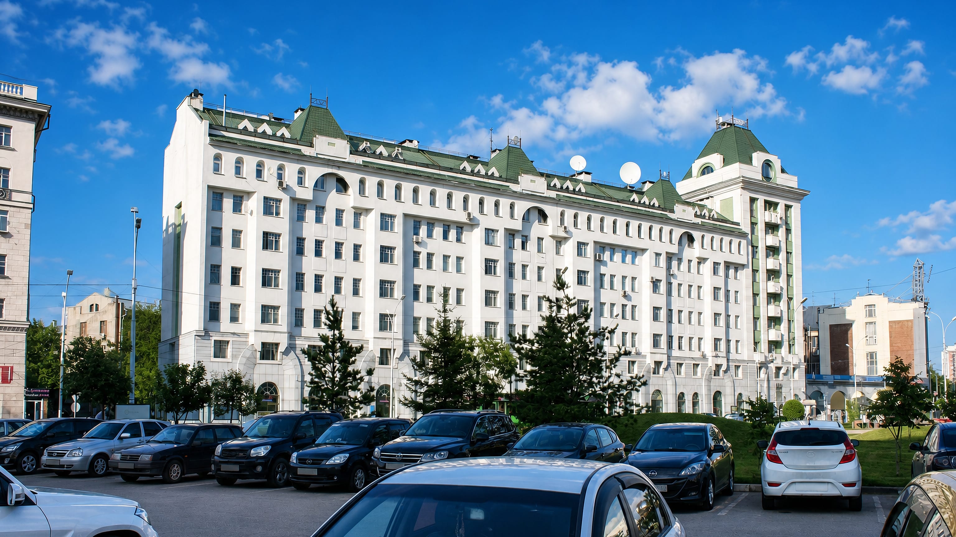 White Stalin-era apartment block with green mansard roofs above a car park in Tsentralny District, Novosibirsk.