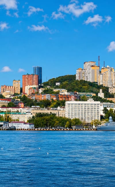 Vladivostok's Golden Horn Bay with a naval warship, hillside city, TV tower and a golden-domed church along the waterfront.