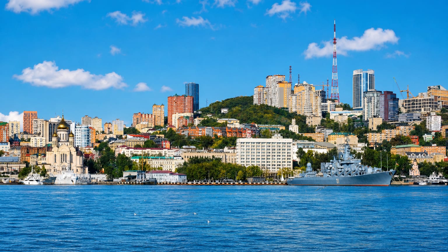 Vladivostok's Golden Horn Bay with a naval warship, hillside city, TV tower and a golden-domed church along the waterfront.