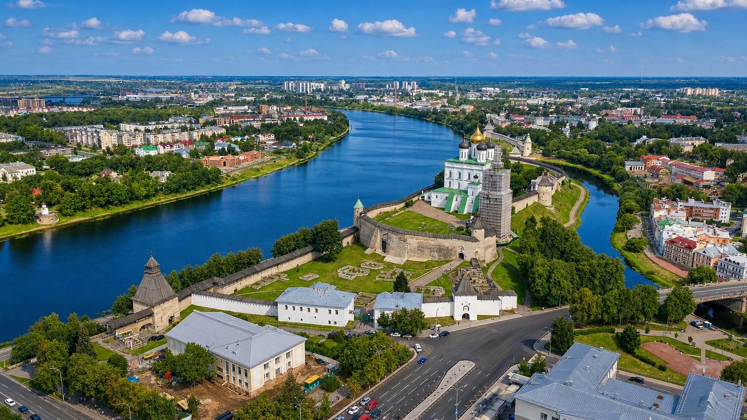 Aerial view of the Pskov Kremlin's white walls and gold-domed cathedral at the river confluence.