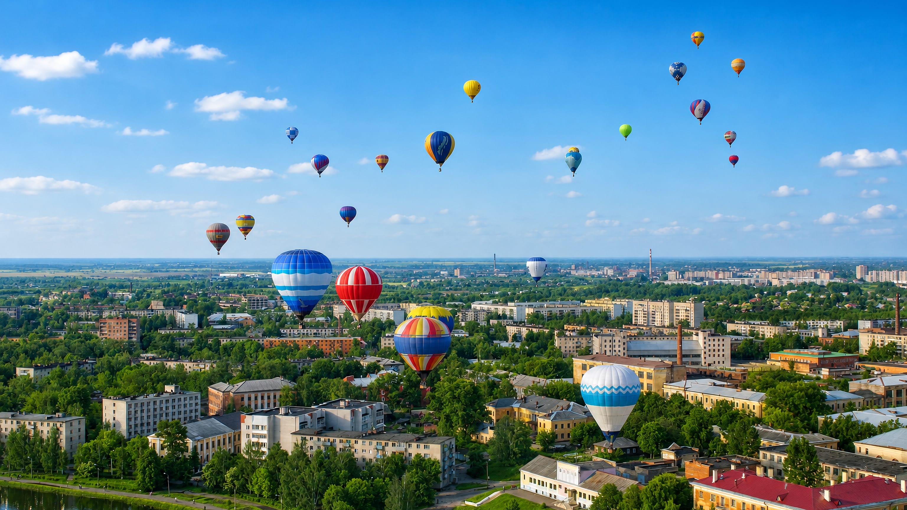Hot-air balloons rising over the low-rise blocks, riverbank and green streets of Velikiye Luki, Russia.