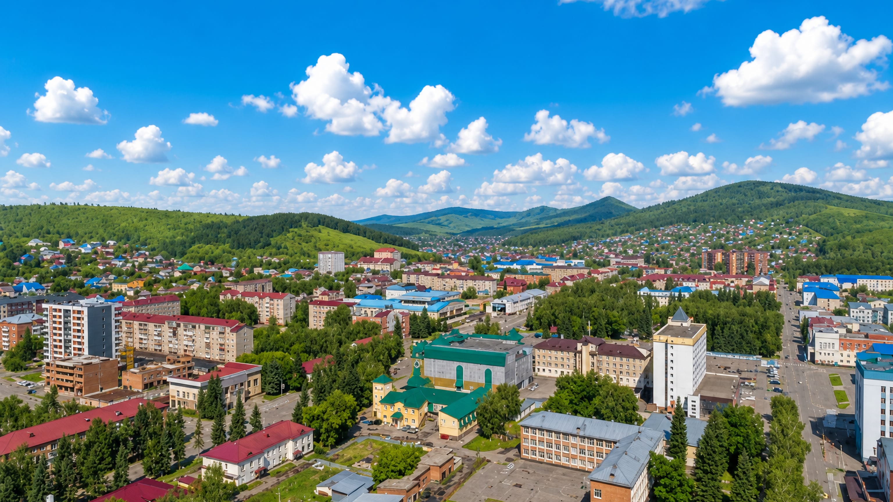 Gorno-Altaysk spread across its green valley, ringed by forested Altai foothills under a bright summer sky.