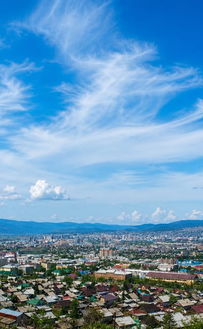 Hilltop panorama of Ulan-Ude, Russia, spread across a valley ringed by low mountains under a bright sky.