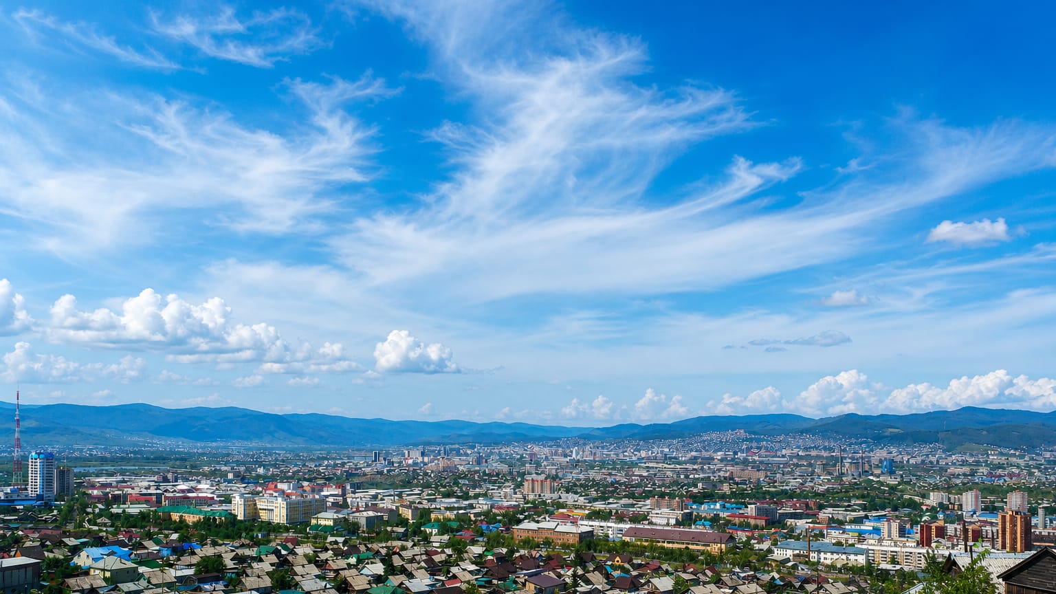 Hilltop panorama of Ulan-Ude, Russia, spread across a valley ringed by low mountains under a bright sky.