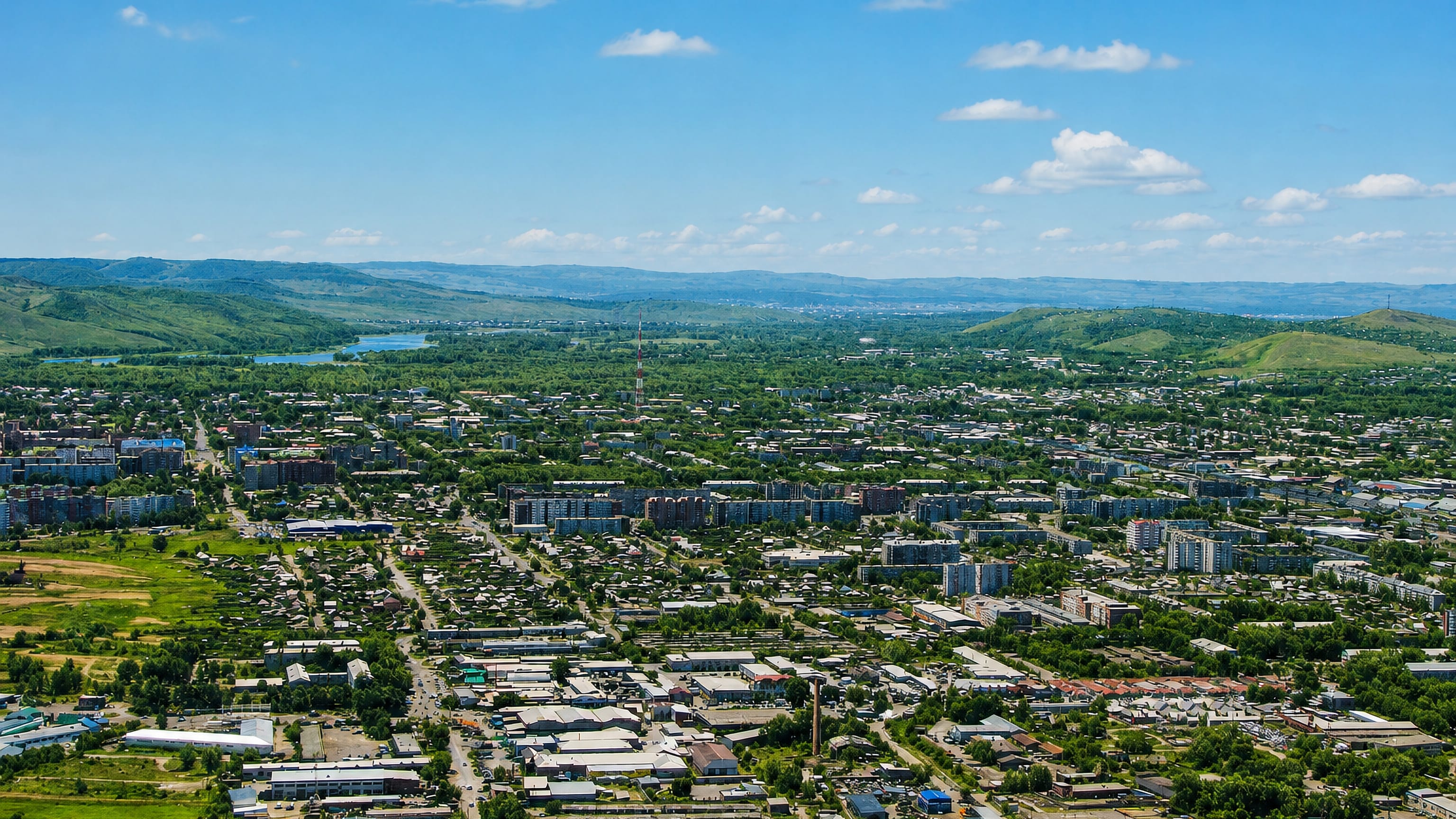 Wide aerial over Abakan, Russia, low-rise streets and apartment blocks spreading toward green Khakassian hills.