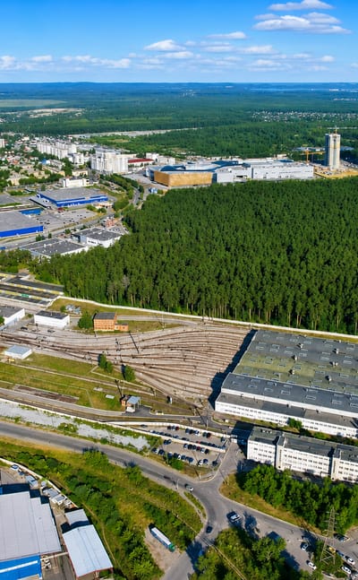Aerial of residential blocks and industrial rail yards beside a vast pine forest in Ozerki, St. Petersburg