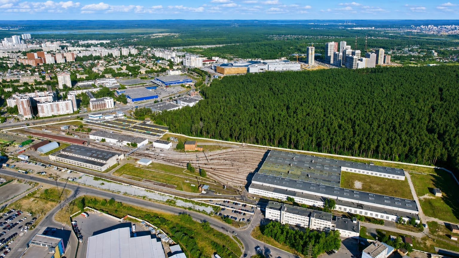 Aerial of residential blocks and industrial rail yards beside a vast pine forest in Ozerki, St. Petersburg