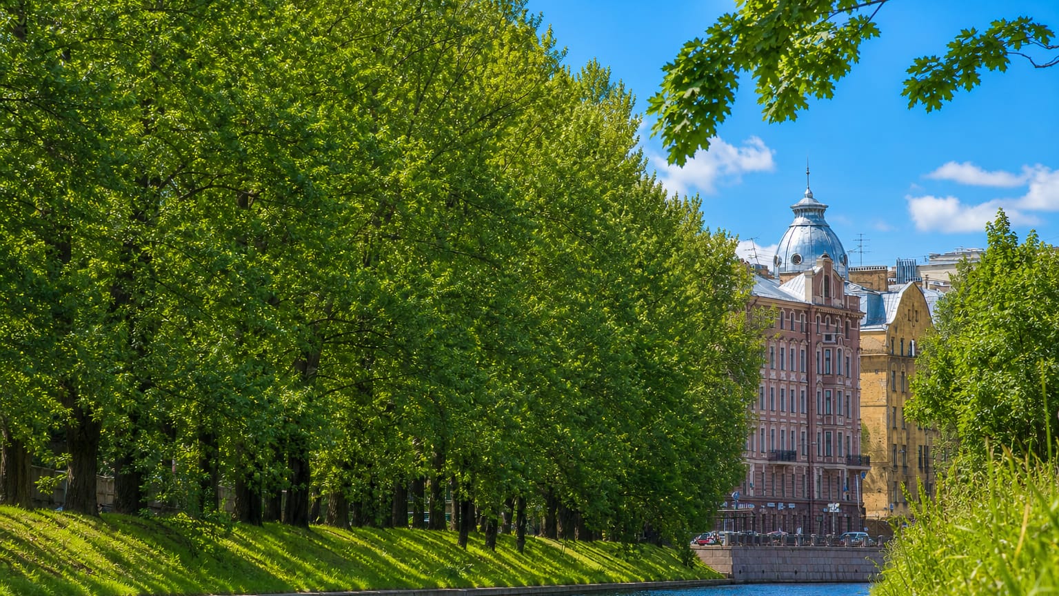 Tree-lined canal with granite embankment and an ornate domed apartment building in Petrogradka, Saint Petersburg