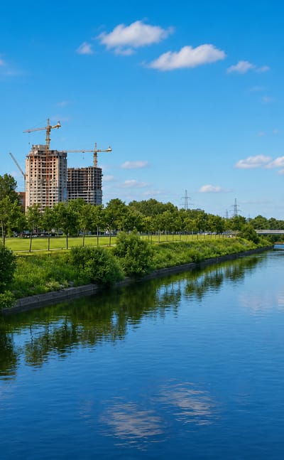 River lined with parkland and trees in Uritsk, St. Petersburg, with a high-rise under construction and a cable-stayed bridge beyond