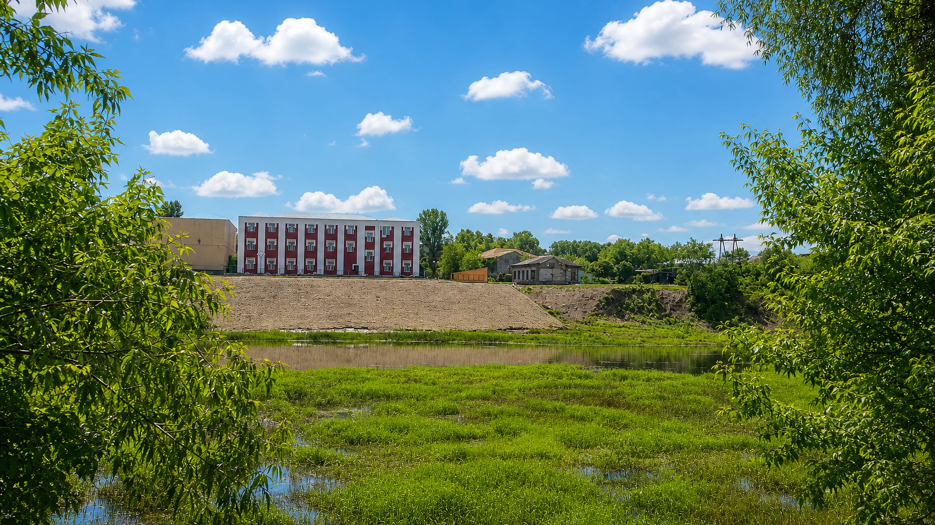 Grassy riverbank of the Khopyor with a red-and-white apartment block on the bluff at Balashov, Russia.