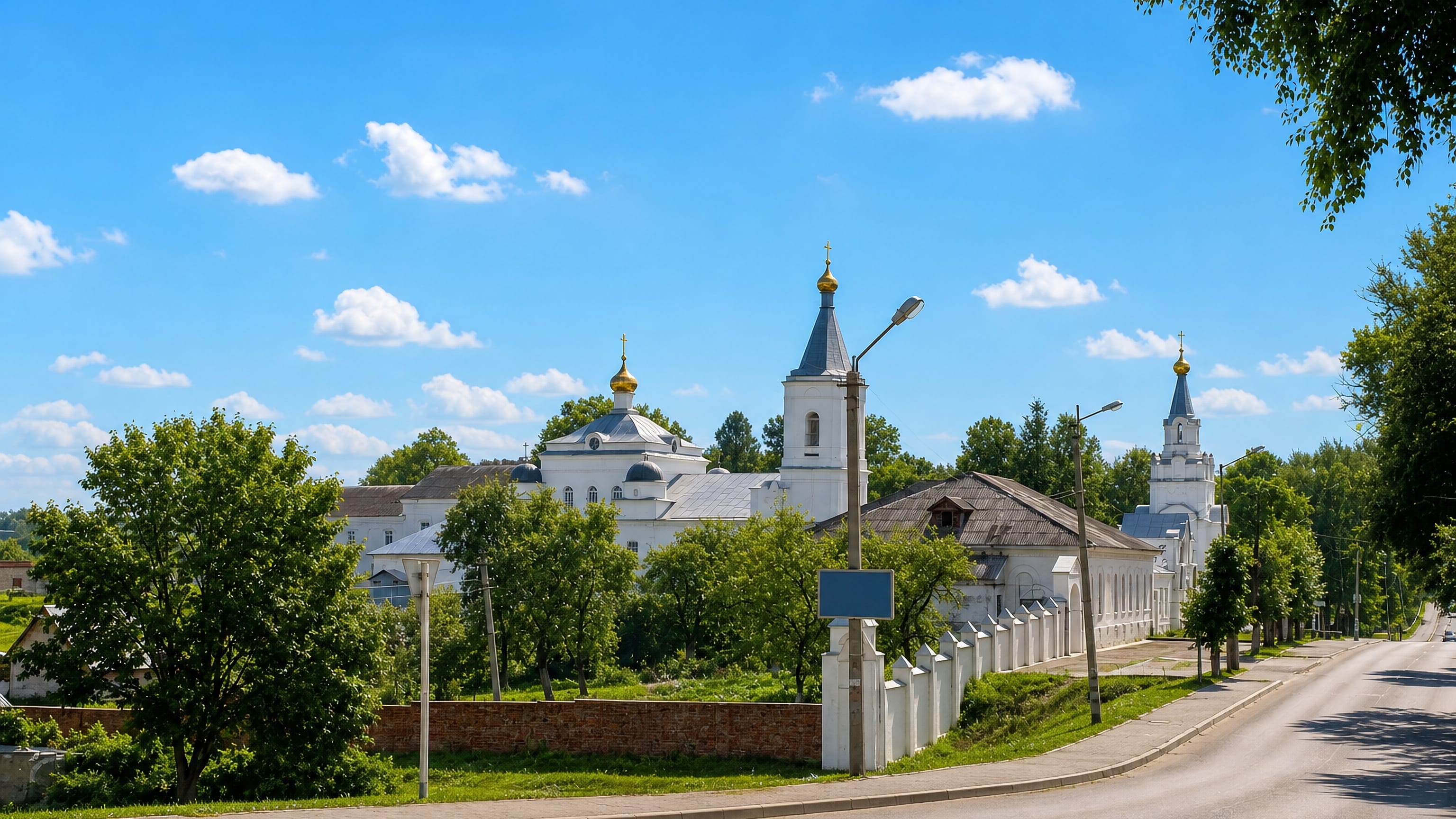 Whitewashed Orthodox monastery church and bell tower beside a quiet summer street in Roslavl, Russia.