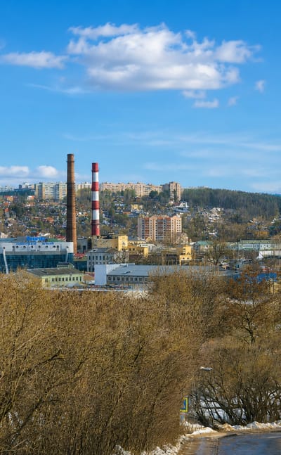 Hillside view over Smolensk, Russia, with residential blocks, a striped industrial chimney and bare early-spring trees