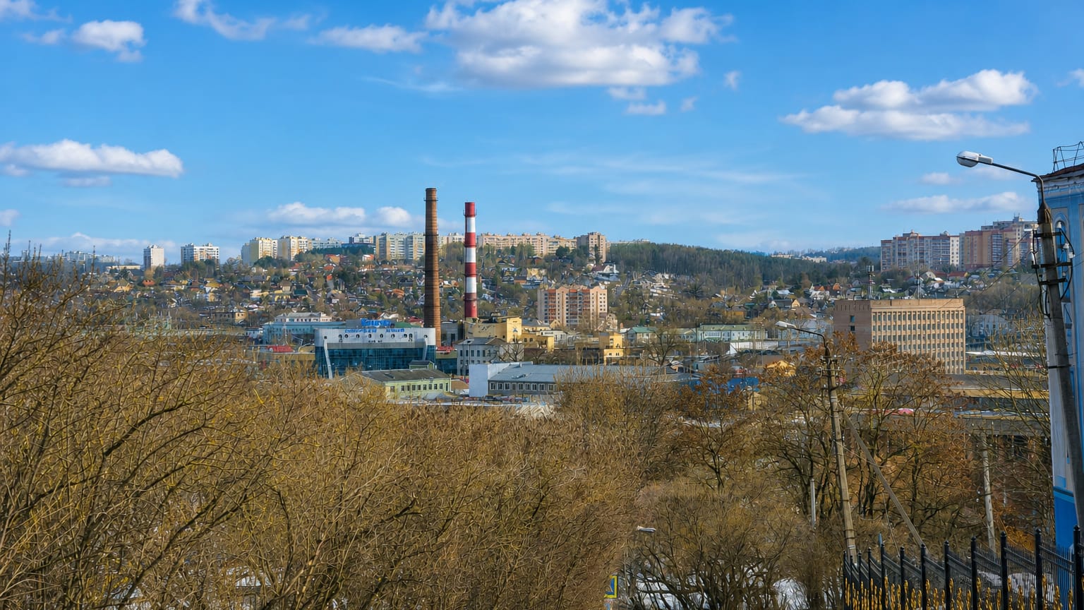 Hillside view over Smolensk, Russia, with residential blocks, a striped industrial chimney and bare early-spring trees