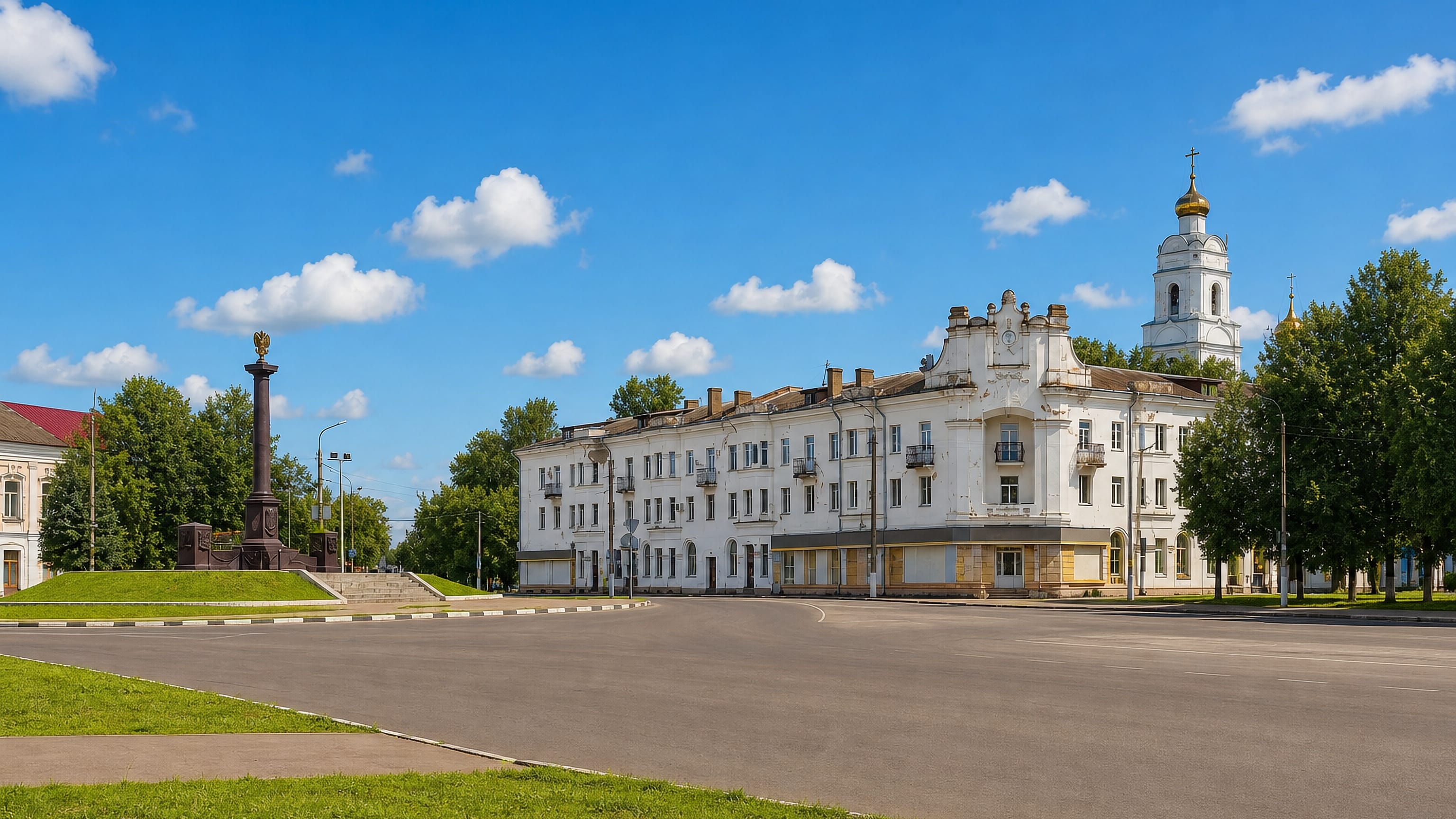 A quiet square in Vyazma with a white Stalin-era block, memorial column and Orthodox bell tower.