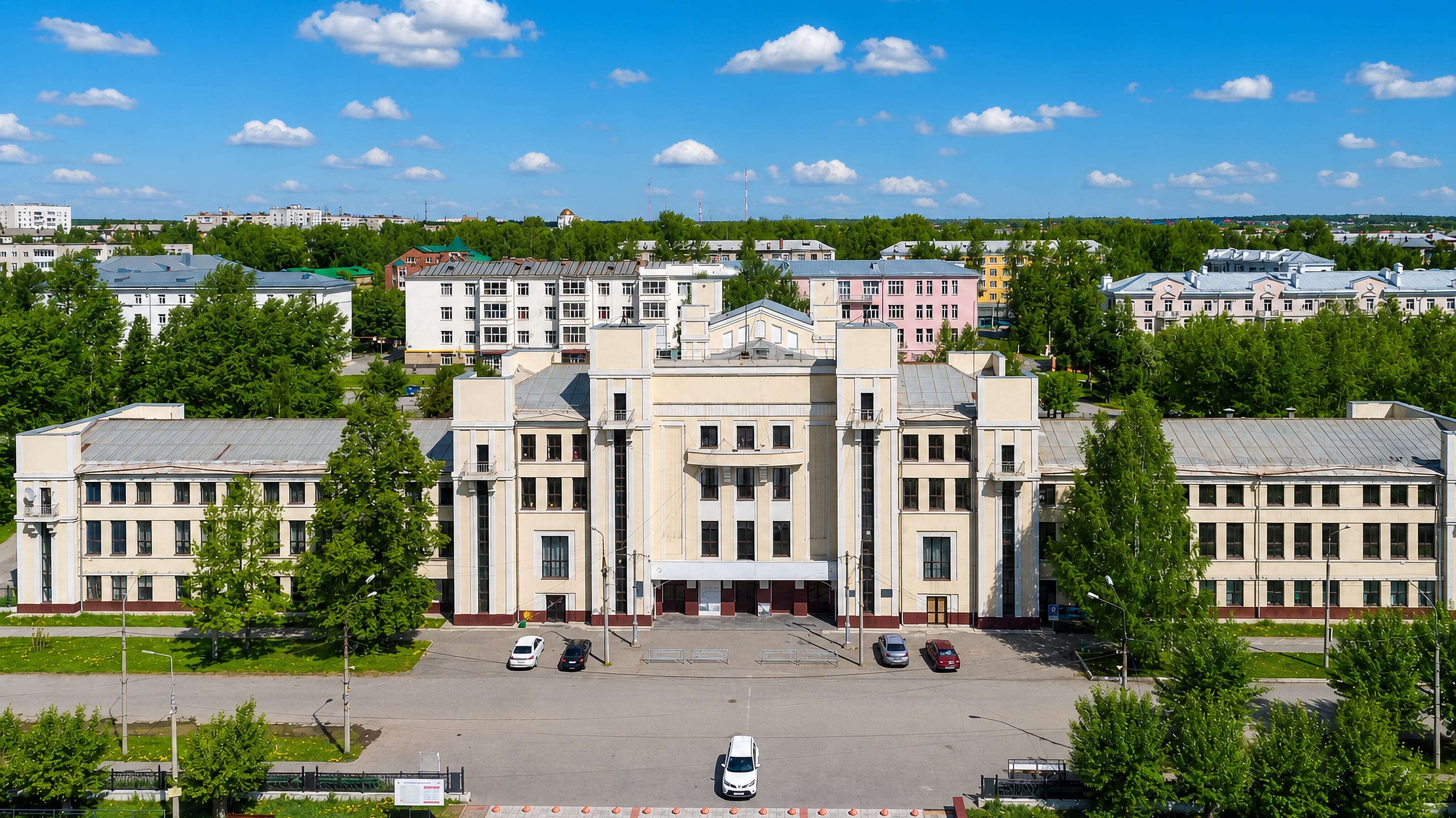 Stalinist palace of culture facing a wide square among Soviet-era blocks and forest in Serov, Russia.