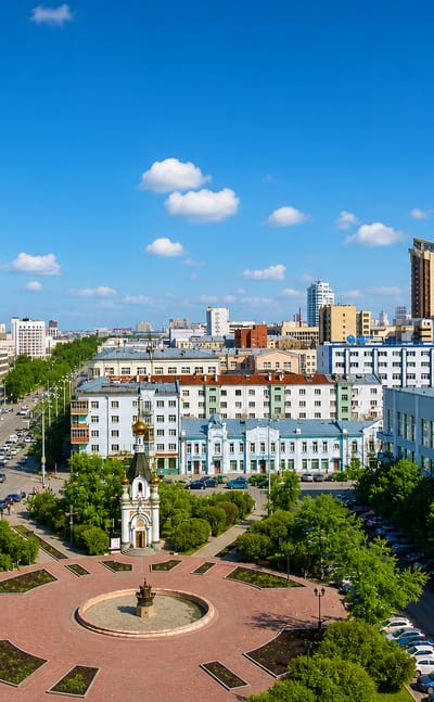 Central Yekaterinburg with the glass Vysotsky skyscraper towering over a boulevard, chapel and circular plaza.