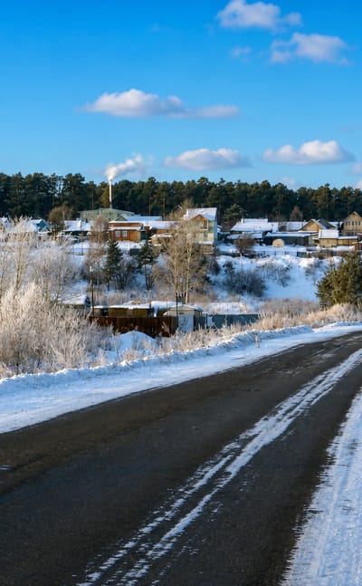 Snow-covered wooden houses and pine forest along the road into Timiryazevskoye near Tomsk on a bright winter day.