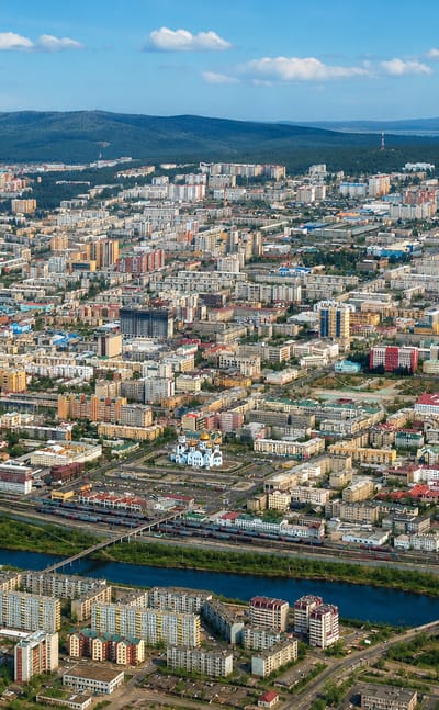 Aerial view of Chita, Russia, with a river and bridge, a golden-domed church and hills on the horizon.