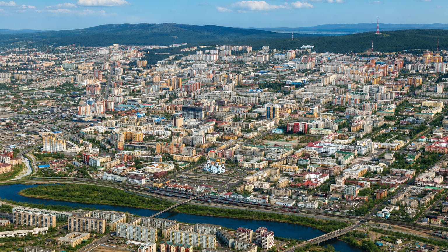 Aerial view of Chita, Russia, with a river and bridge, a golden-domed church and hills on the horizon.