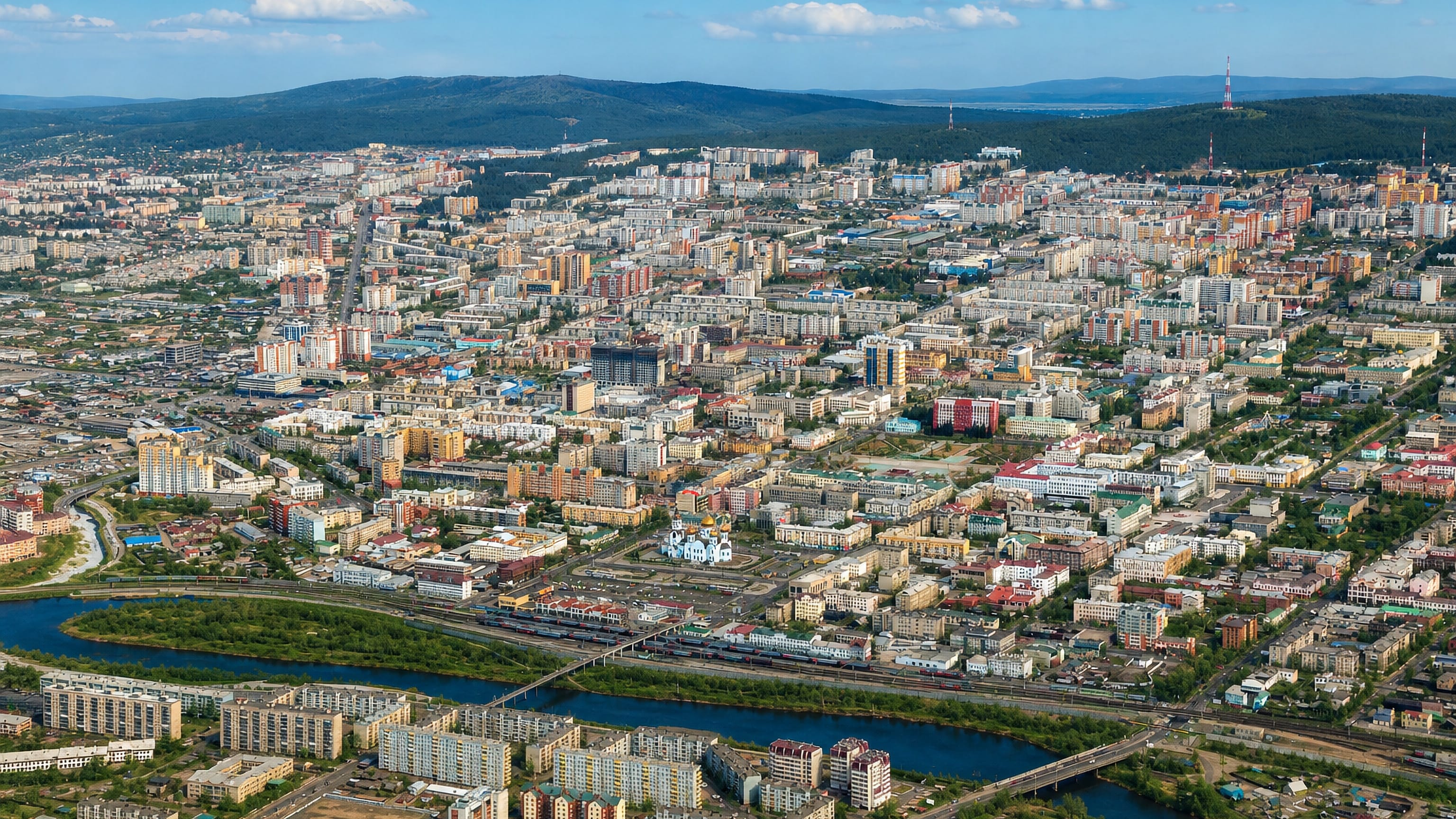 Aerial view of Chita, Russia, with a river and bridge, a golden-domed church and hills on the horizon.