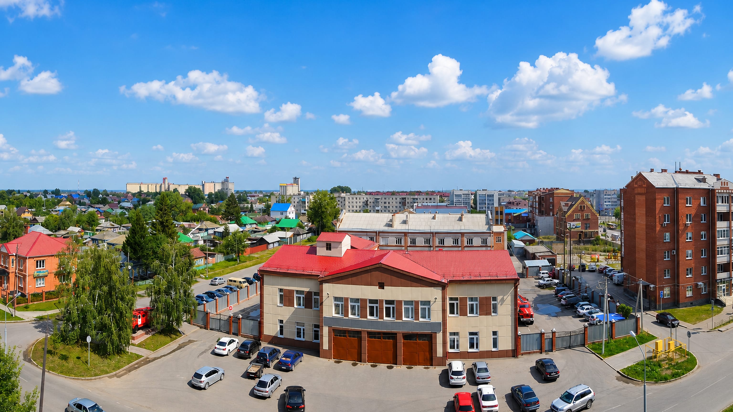 Red-roofed civic building, low-rise streets and distant grain elevators seen from above in Ishim, Russia.
