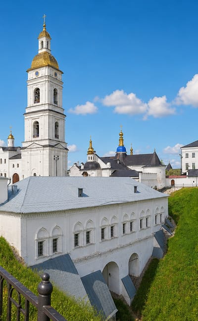 White walls, golden bell tower and blue-domed cathedral of the Tobolsk Kremlin above green ramparts, Russia.