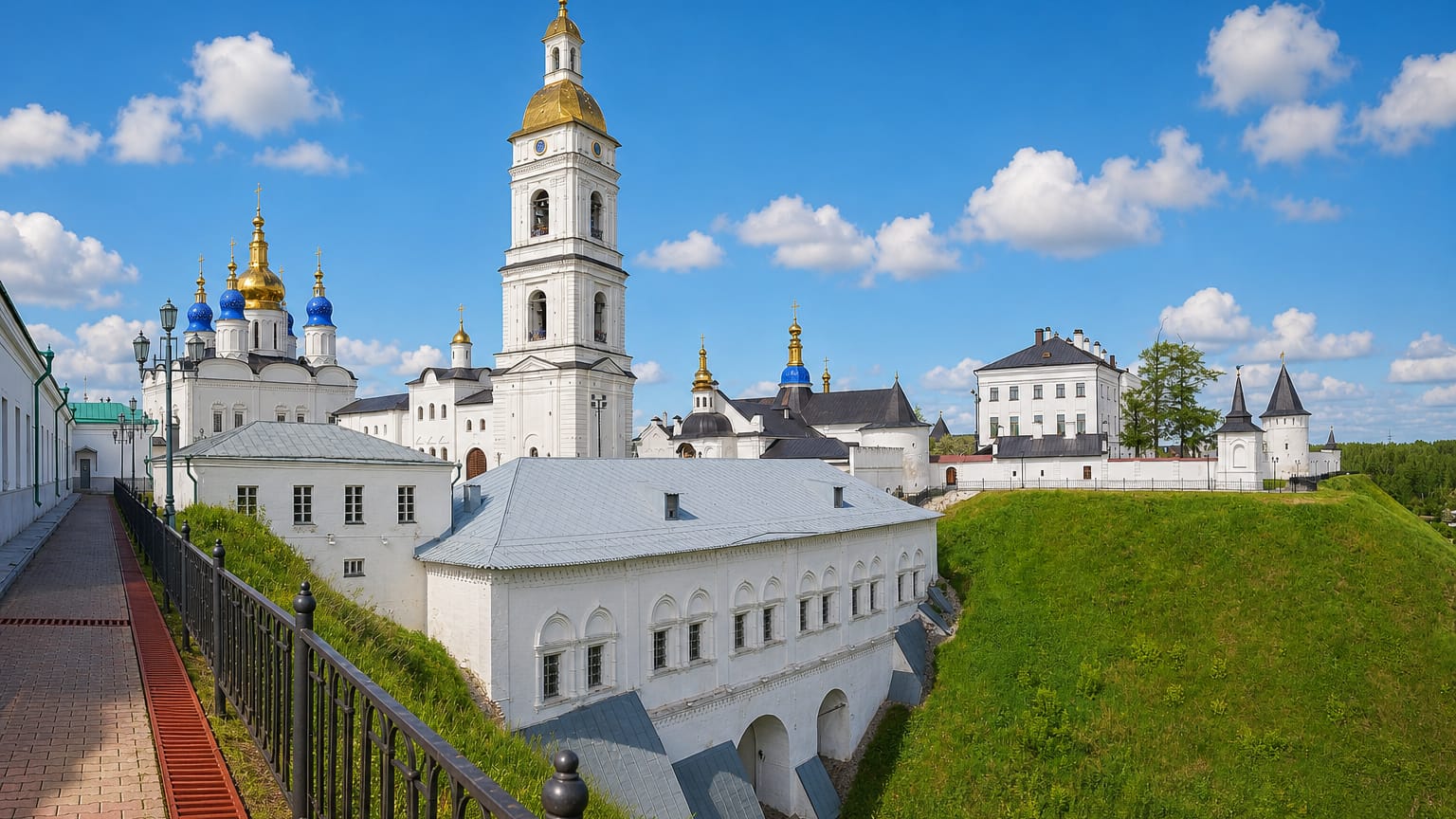 White walls, golden bell tower and blue-domed cathedral of the Tobolsk Kremlin above green ramparts, Russia.
