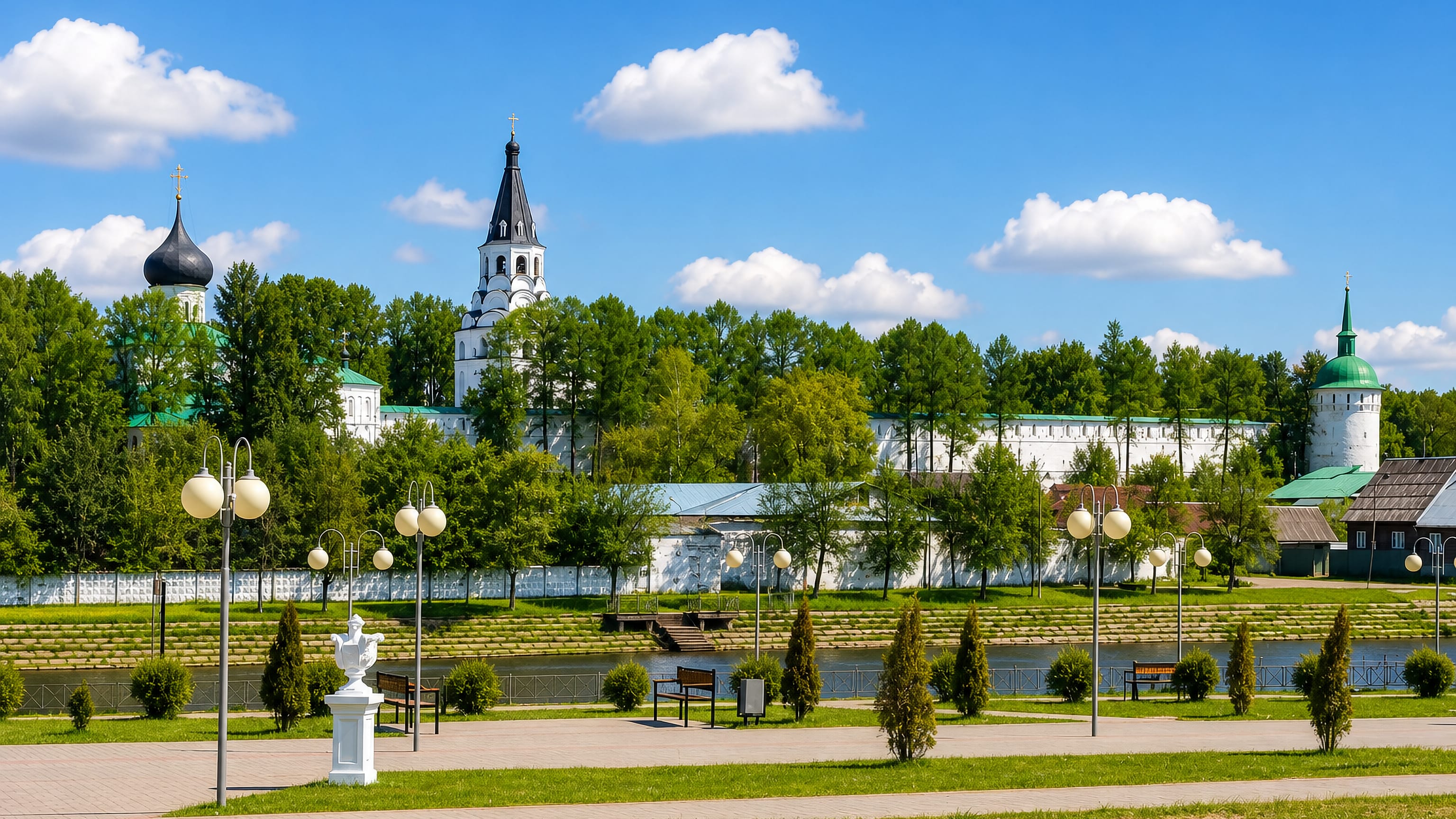 White walls, bell tower and onion domes of the Alexandrov Kremlin above the riverside promenade in Aleksandrov, Russia.