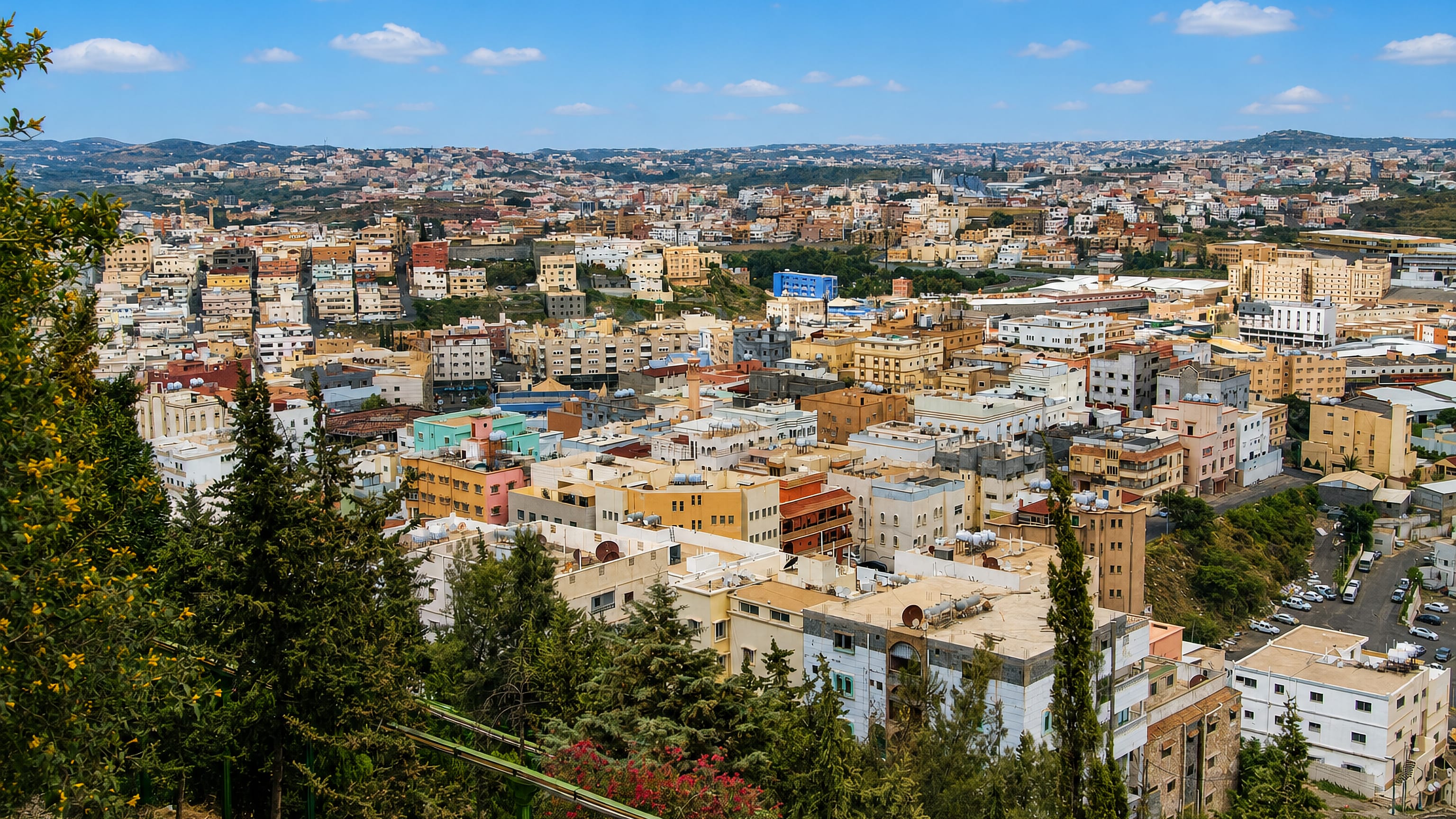 Abha, Saudi Arabia, its pastel hillside buildings spread across the Asir highlands seen through juniper trees.