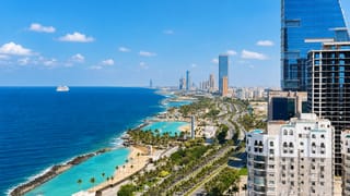 Jeddah's Corniche waterfront along the turquoise Red Sea with palm-lined boulevard and modern skyscrapers.