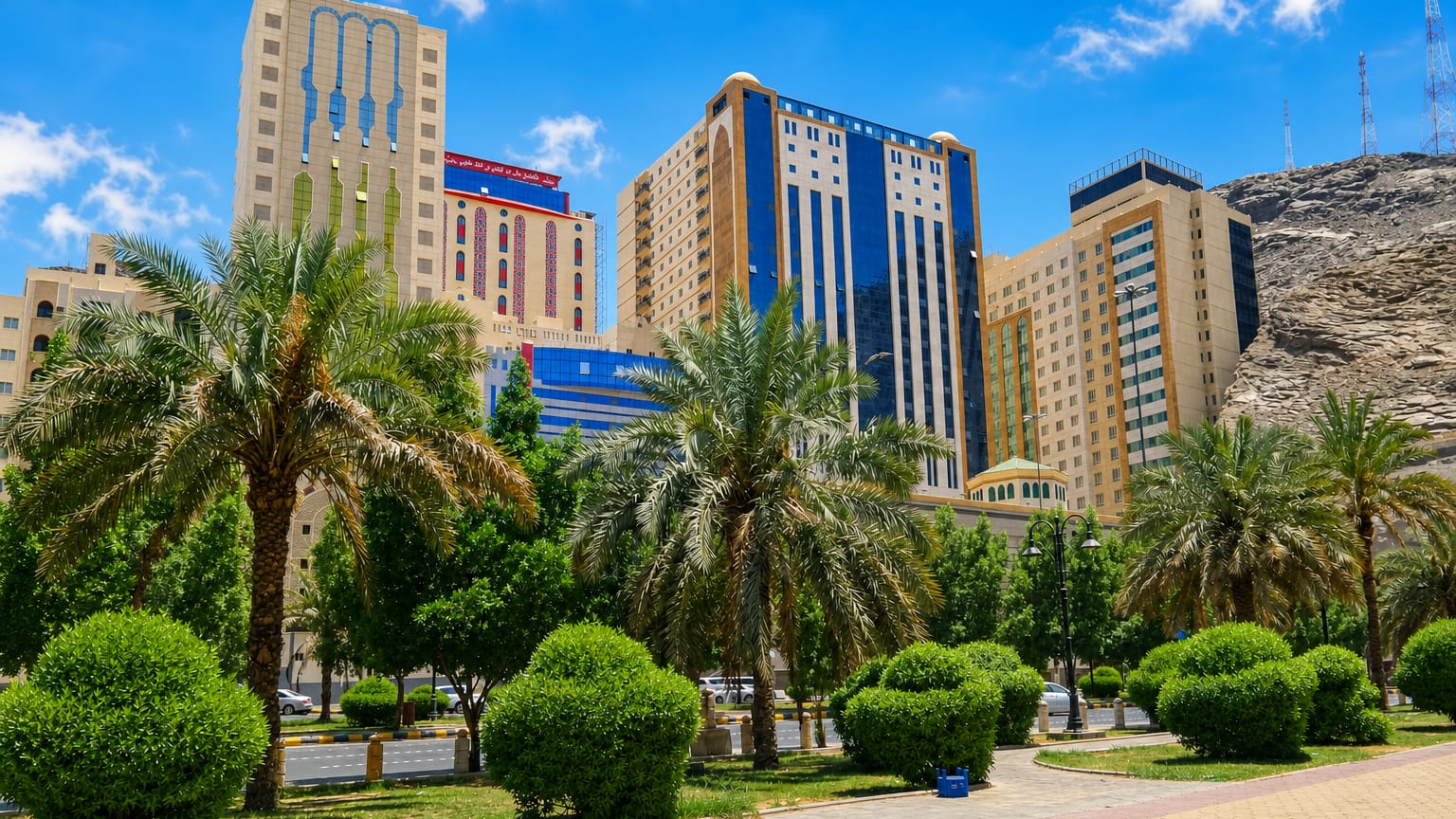 Ajyad district in Makkah with palm-lined gardens, mid-rise hotel towers and a bare rocky mountain behind under a bright sky