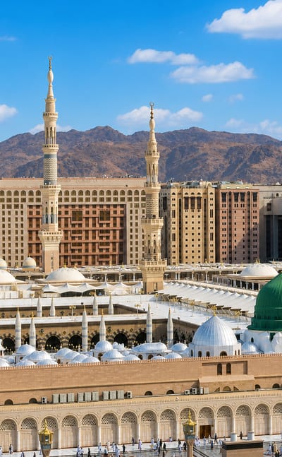 Al-Masjid an-Nabawi with its green dome, minarets and courtyard umbrellas in Medina against mountains