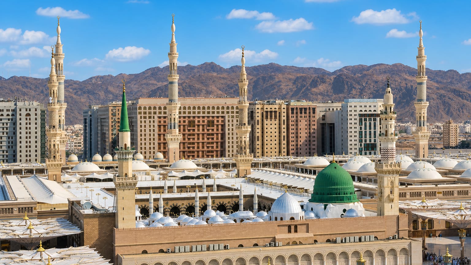 Al-Masjid an-Nabawi with its green dome, minarets and courtyard umbrellas in Medina against mountains