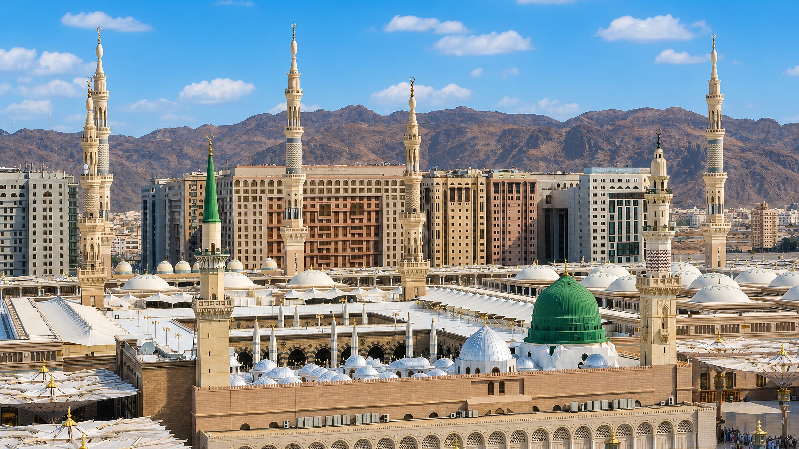 Al-Masjid an-Nabawi with its green dome, minarets and courtyard umbrellas in Medina against mountains
