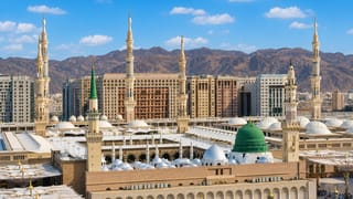 Al-Masjid an-Nabawi with its green dome, minarets and courtyard umbrellas in Medina against mountains