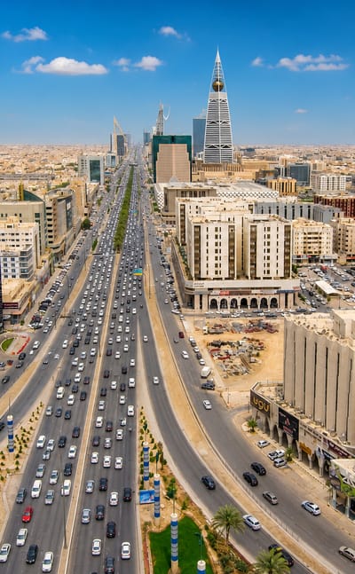 Riyadh's King Fahd Road with heavy traffic and the Al Faisaliah and Kingdom towers rising in the skyline.