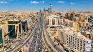 Riyadh's King Fahd Road with heavy traffic and the Al Faisaliah and Kingdom towers rising in the skyline.