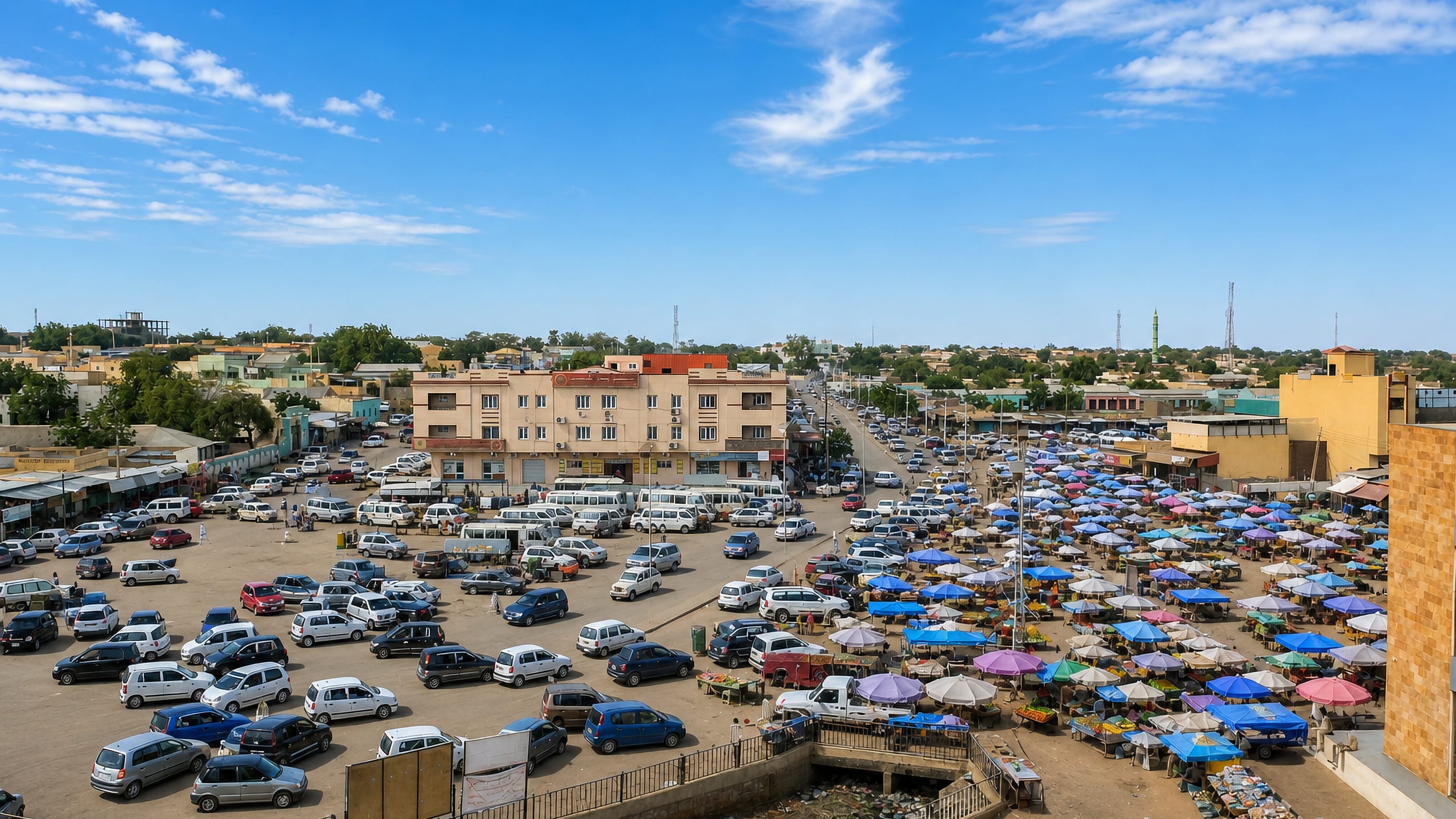 Market square in El Fasher, Sudan, packed with parked vehicles and rows of colourful stall umbrellas