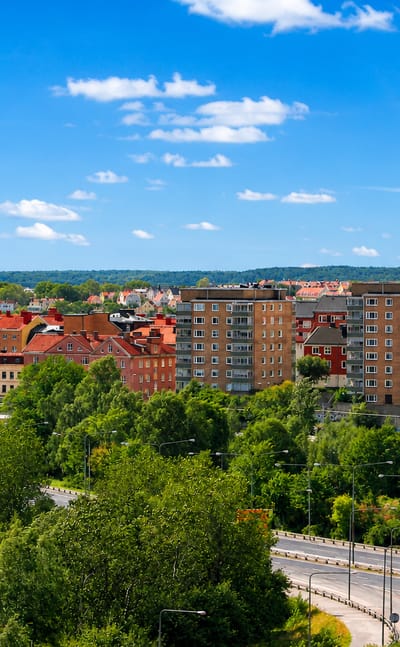 Pantarholmen district in Karlskrona, Sweden, with red-roofed apartment blocks, greenery and archipelago water beyond under a blue sky.